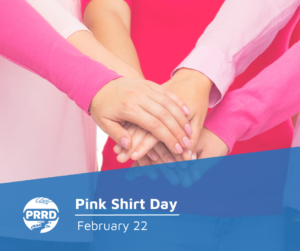 A circle of hands placed om top of each other to show support, with the people dressed in pink shirts